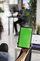 Entrepreneur holding tablet with chroma key screen to chat in video call in coworking space. Company employee using digital device with green touchscreen in business office photo