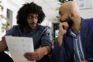 Executive manager and colleague brainstorming while analyzing report together in business office. Financial analysts checking papers with sales result statistics in coworking space photo