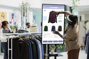 Male customer using clothing store kiosk service, choosing fashion collection items online on self ordering checkout board. Young adult slectiong clothes on interactive monitor display. photo