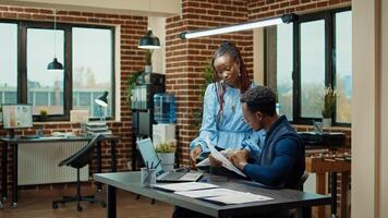 African american people planning report with annual data on papers and laptop, using online statistics to plan business development. Man and woman reviewing startup results in boardroom. photo