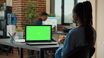 Manager working with greenscreen in business office, looking at blank chroma key display. Company employee using isolated mockup template and copyspace on laptop, coworking space. Tripod shot. photo