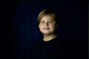 A concise portrait of a European boy. Portrait on a dark background. photo