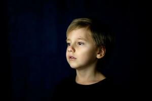 A concise portrait of a European boy. Portrait on a dark background. photo