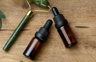 Brown glass bottle with a pipette,  stone hand massager for cosmetic procedures on a wooden background photo