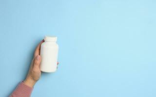 Two female hands holding a white plastic bottle for pills on a blue background photo