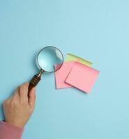 Empty paper stickers adhered to a blue background, and a female hand with a magnifying glass photo