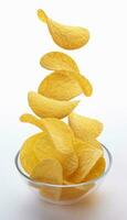 Potato chips falling into glass bowl isolated on white background photo