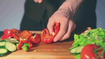 cocinero en negro uniforme es rebanar rojo pimenton y preparando vegetal ingredientes para cocinando. hombre en un cocina es corte rojo pimienta para vegetariano plato. sano comida concepto lento movimiento video