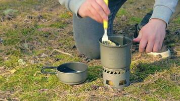 homme dans une forêt est cuisine Pâtes en utilisant une petit cuisinier ensemble. promeneur dans une forêt est préparation pour le déjeuner. statique fermer coup video