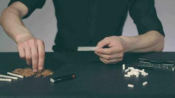 Man in Black Clothing is Rolling a Hand Made Cigarette Using Papers, Filters and Tobacco. A Way to Save on Tobacco Products. Tobacco Product Economy Concept Slow Motion video