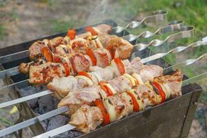 Grilled pieces of meat on skewers, shish kebab with vegetables, cooking process on brazier photo
