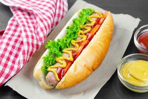 Homemade Hot Dog with mustard, ketchup, tomato and fresh salad leaves on black slate background photo