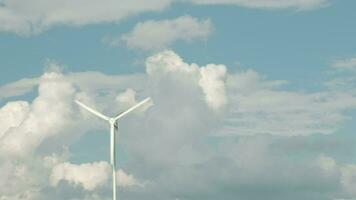 uma branco moinho de vento dentro azul céu e nuvens fundo, virar dentro vento para gerar limpar \ limpo elétrico energia indústria, natural poder recurso tecnologia para sustentável ecologia e meio Ambiente conservação. video