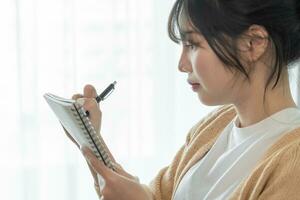 Asian Business woman working from office taking reading and writing notes in note pad photo