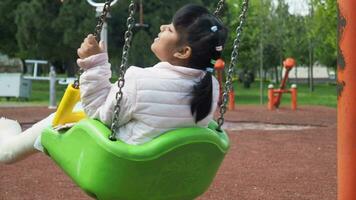 bambino avendo divertimento su un' swing su il terreno di gioco nel pubblico parco. video