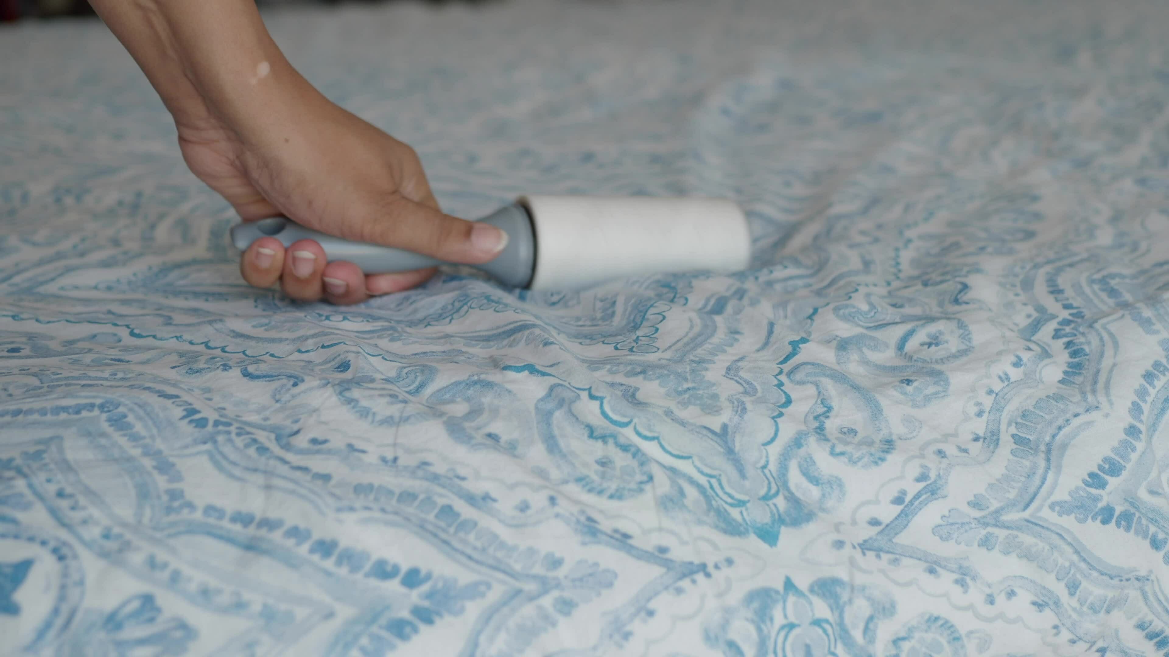 using an adhesive roller to remove lint and fluff from a bed . 35719512