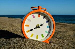 an orange clock on the beach with the ocean in the background photo