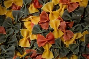 Uncooked Vibrant Colored Farfalle Pasta. A Culinary Canvas of Multicolored Bow-Tie Macaroni, Creating a Lively and Textured Background for Gourmet Cooking Enthusiasts. Colored Dry Pasta. Raw Macaroni photo