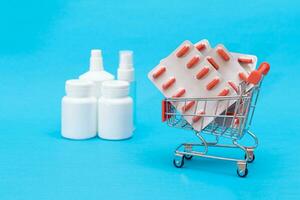 Buying Medicines. Expensive Medicine and Inflation Concept. Pills and Capsules in Shopping Cart on Blue Background. Global Pharmaceutical Industry and Big Pharma. Ordering Pharmaceutical Products photo