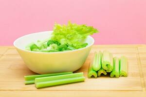 Fresh Chopped Celery Slices in White Bowl with Celery Sticks on Bamboo Cutting Board. Vegan and Vegetarian Culture. Raw Food. Healthy Diet with Negative Calorie Content photo
