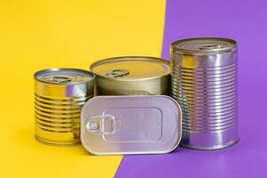 A Group of Stacked Tin Cans with Blank Edges on Split Yellow and Violet Background. Canned Food. Different Aluminum Cans for Safe and Long Term Storage of Food. Steel Sealed Food Storage Containers photo