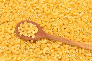 Uncooked Chifferi Rigati Pasta Background with Wooden Spoon. Fat and Unhealthy Food. Classic Dry Macaroni. Italian Culture and Cuisine. Raw Pasta photo