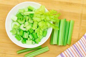 Fresh Chopped Celery Slices in White Bowl with Celery Sticks on Bamboo Cutting Board. Vegan and Vegetarian Culture. Raw Food. Healthy Diet with Negative Calorie Content photo