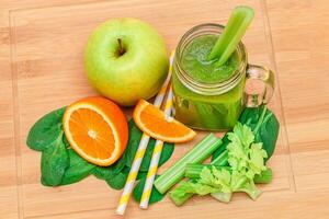 Fresco verde zalamero de manzana, apio, Espinacas y naranja en vaso zalamero tarro con amarillo cóctel Paja en de madera corte tablero. vegano desintoxicación beber. vegetariano cultura. sano comiendo y Fruta dieta foto