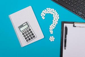 Treatment Costs and Budget. Question Mark Made from White Pills and Tablets with Calculator and Notepad, Lying on Blue Background. Global Pharmaceutical Industry and Medicinal Products photo