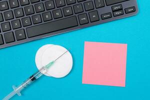 Vaccination, Immunology or Revaccination Concept A Medical Disposable Syringe Lying on Blue Table in Doctor's Office in a Hospital or Clinic. Blank Pink Sticky Note Mock Up with Copy Space photo