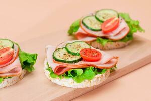 Light Breakfast. Quick and Healthy Sandwiches. Rice Cakes with Ham, Tomato, Fresh Cucumber and Green Salad on Wooden Cutting Board. Beige Background photo