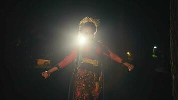 an Asian woman walks while dancing in front of the lights while wearing a bun in her black hair with gold accessories video