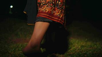 ett asiatisk kvinnas ben är dans mycket flexibelt på de grön gräs medan bär en batik kjol video