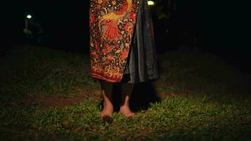 An Asian woman's legs are dancing very flexibly on the green grass while wearing a batik skirt video