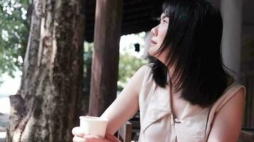 souriant asiatique femme est en buvant une chaud de café et relaxant dans Naturel jardin video