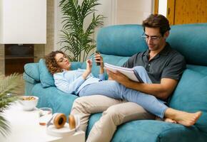 Positive couple resting on sofa while bonding and working in living room photo