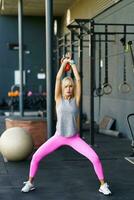 ajuste joven mujer haciendo sentadillas ejercicios con pesas rusas en gimnasio foto