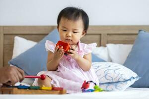 Adorable little asian baby toddler is sitting on the bed playing wooden melody toy for preschool learning and growth development concept photo