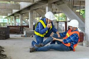 asiático fábrica trabajador teniendo accidente mientras trabajando en fabricación sitio mientras su colega es Ayudar para la seguridad lugar de trabajo y emergencia foto