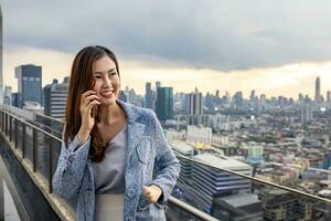 Asian business woman in formal suit is phone calling customer while standing outside the skyscraper building for marketing, connection, corporate work, real estate, housing and urban development photo