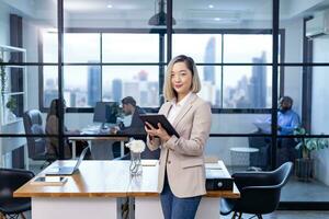 Portrait of Asian business CEO woman is standing in the office at the table with digital tablet and showing statistic chart showing annual report and skyscraper background photo