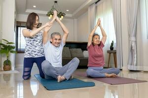 Senior asian couple is exercising at home doing sitting meditation yoga pose with her trainer daughter encourage and cheering for elder healthy concept photo