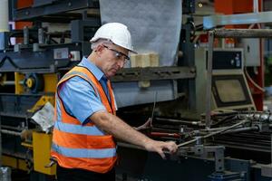 caucásico industrial trabajador es utilizando ordenador portátil computadora a calibrando el máquina mientras inspeccionando dentro el metal sábana galvanizado techo fábrica para la seguridad industria foto