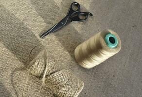 Yellow skeins of thread and scissors on a background of burlap. Yellow coarse cloth threads and scissors. photo