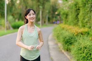 Fit Asian young woman jogging in park smiling happy running and enjoying a healthy outdoor lifestyle. Female jogger. Fitness runner girl in public park. healthy lifestyle and wellness being concept photo