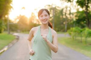 Fit Asian young woman jogging in park smiling happy running and enjoying a healthy outdoor lifestyle. Female jogger. Fitness runner girl in public park. healthy lifestyle and wellness being concept photo