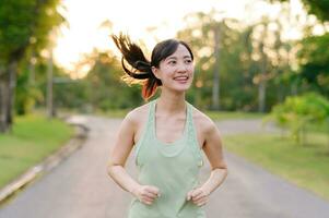 ajuste asiático joven mujer trotar en parque sonriente contento corriendo y disfrutando un sano al aire libre estilo de vida. hembra persona que practica jogging. aptitud corredor niña en público parque. sano estilo de vida y bienestar siendo concepto foto