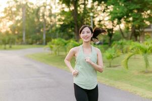 Fit Asian young woman jogging in park smiling happy running and enjoying a healthy outdoor lifestyle. Female jogger. Fitness runner girl in public park. healthy lifestyle and wellness being concept photo