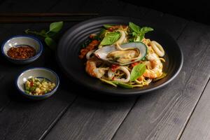 Seafood drunken spaghetti with shrimp squid clams chili, and basil. Thai food. Healthy Asian in a plate on a black background table. Top view. photo