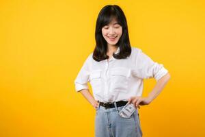 Captivating image of Asian young woman wearing white shirt and denim jeans, confidently holding cash from her shirt pocket. Fashion meets financial empowerment. Perfect for finance and fashion themes. photo